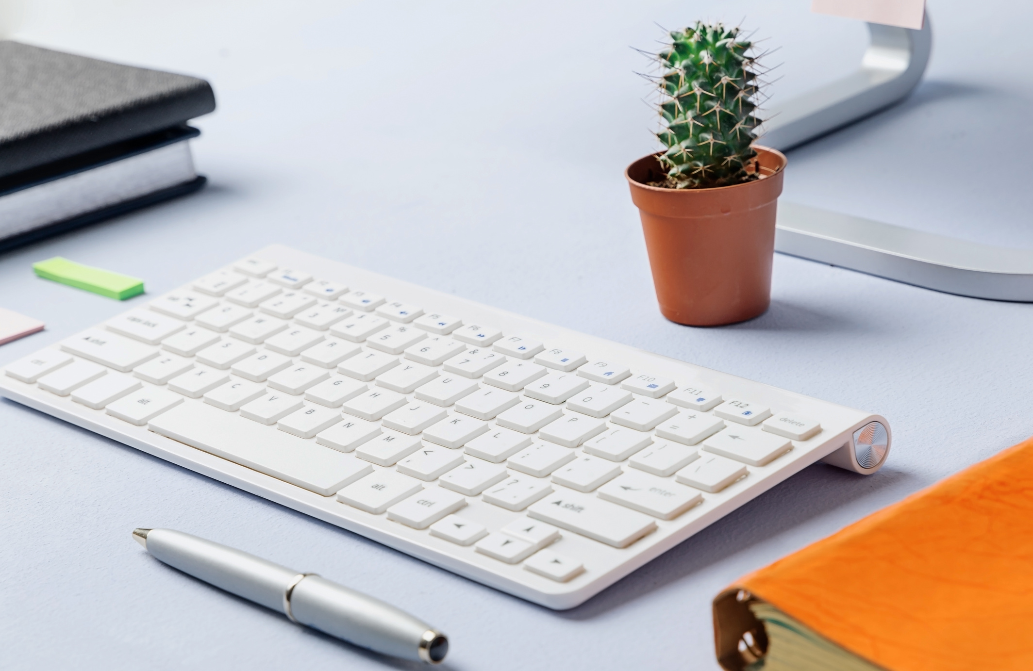 Modern desktop close up. White keyboard, cactus, notebook and pen metal, on a blue table. Copywriting concept